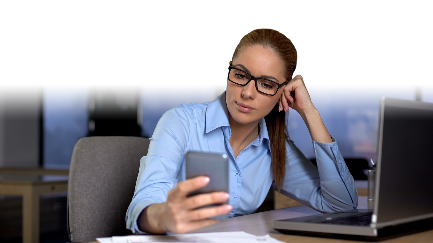 Employee at her desk distracted by her phone instead of her laptop